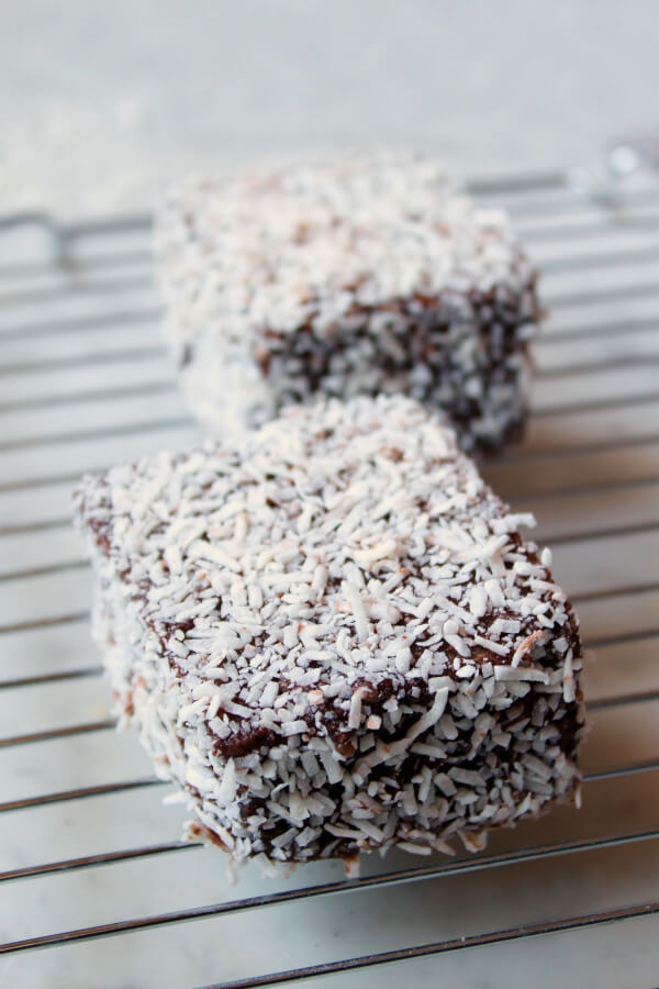 Two chocolate and coconut covered lamingtons on a rack.