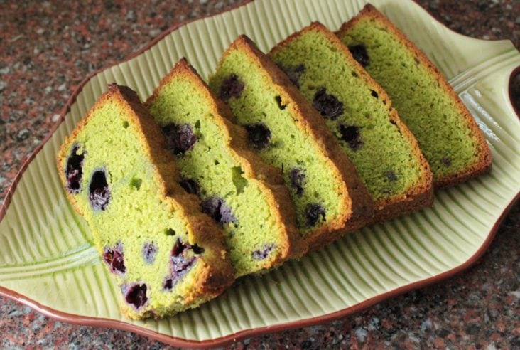 A green loaf cake studded with purple blueberries