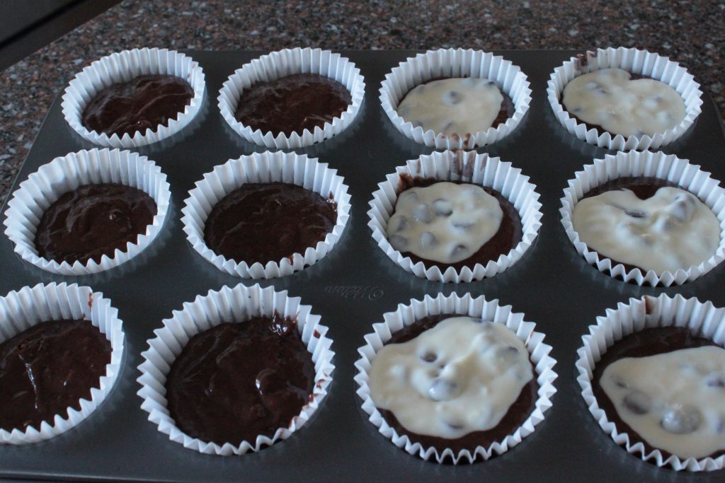 A muffin pan filled with batter and cream cheese filling. 