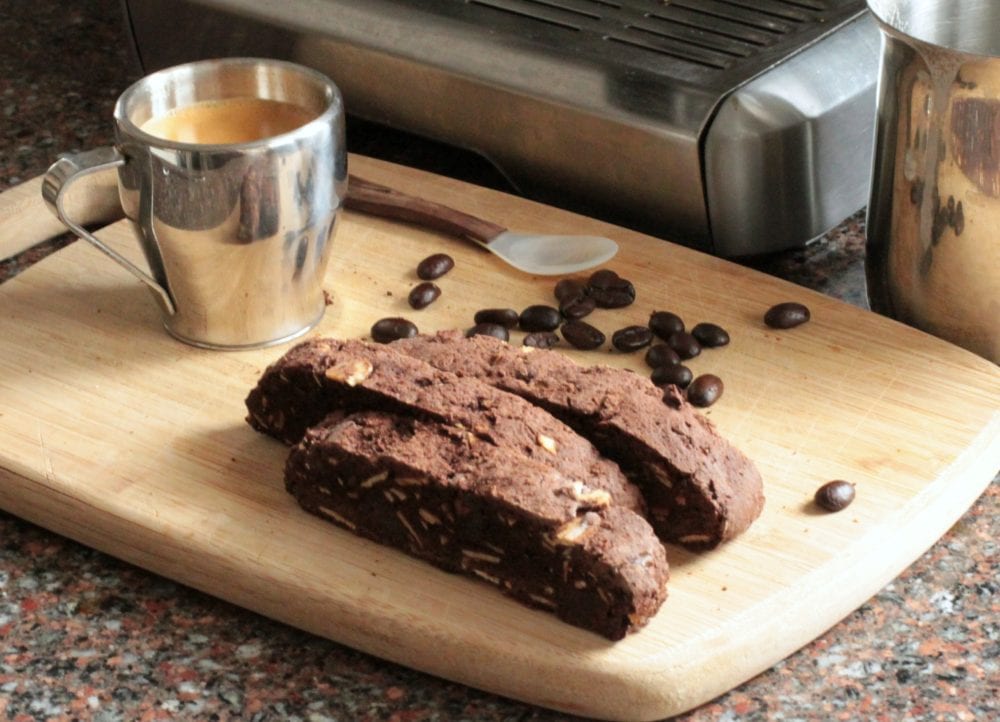 Sliced Chocolate Almond Biscotti on a wooden board in front of an espresso machine.
