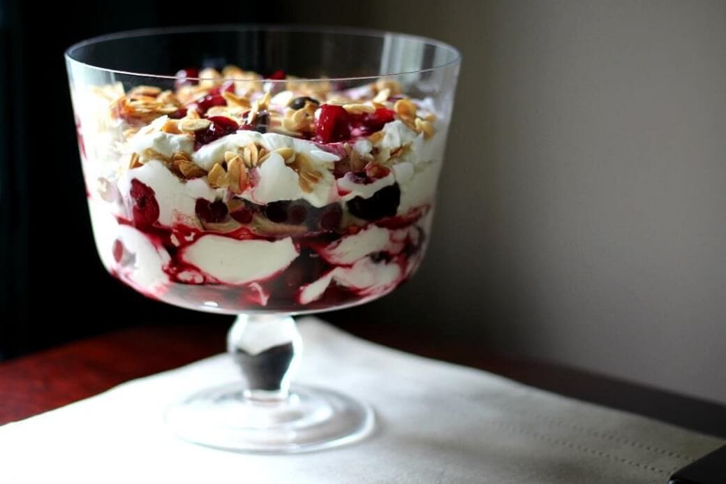 A trifle bowl filled with bright red cherries, whipping cream and almonds.
