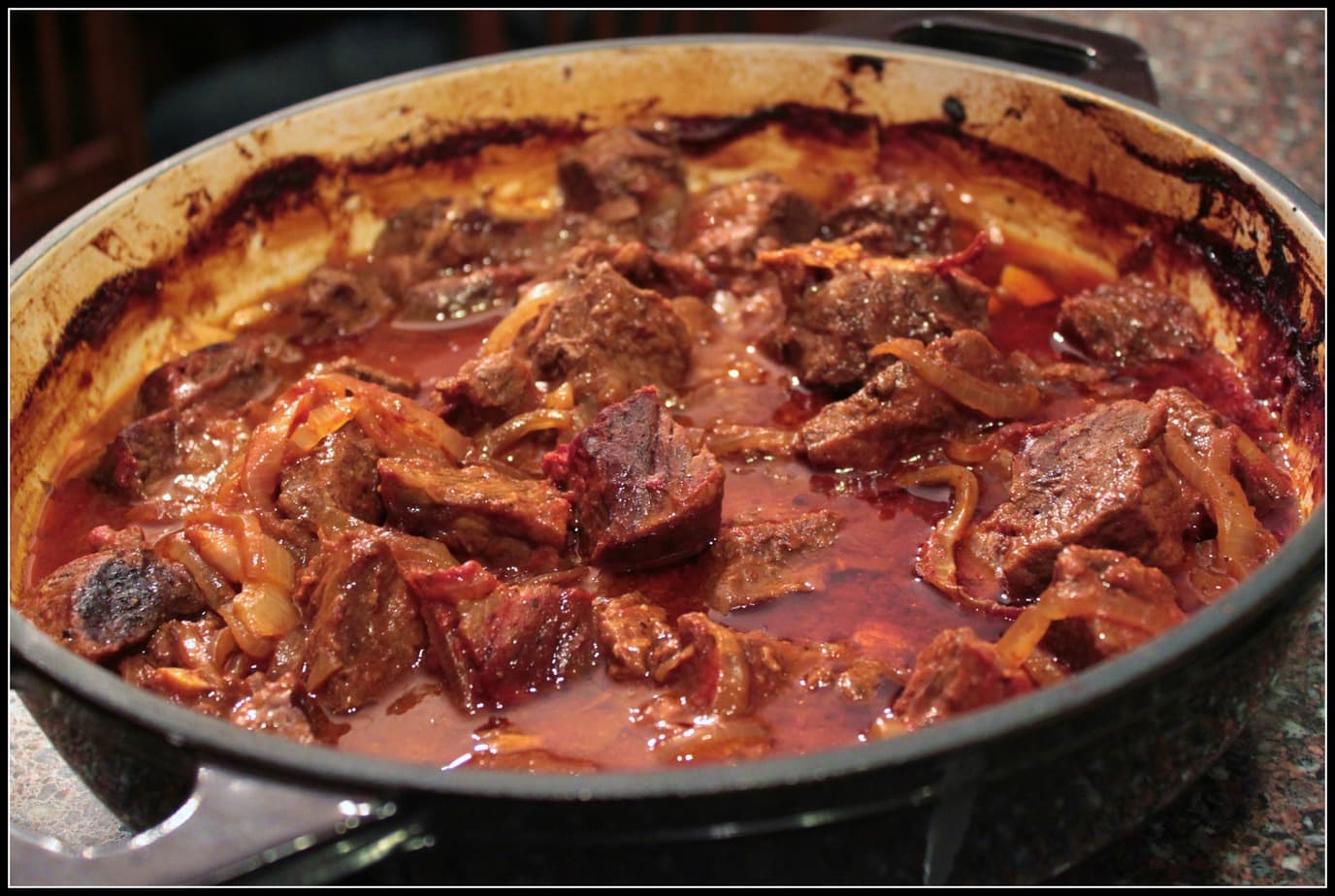 A Dutch oven filled with rich wild meat goulash in a tomato and onion sauce.