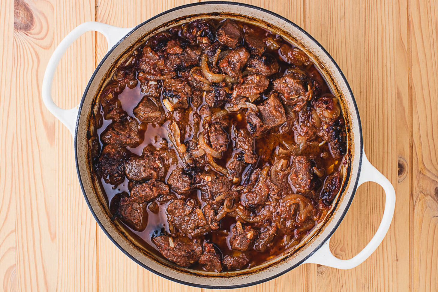 A Dutch oven filled with rich wild meat goulash in a tomato and onion sauce.