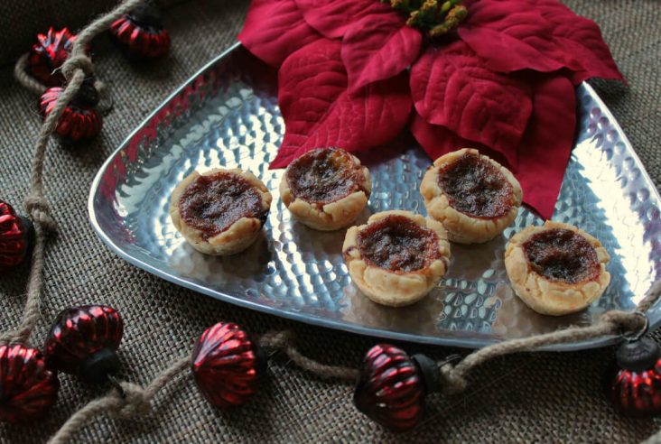 Butter Tarts on a silver serving tray surrounded by a red poinsetta and Christmas decorations.