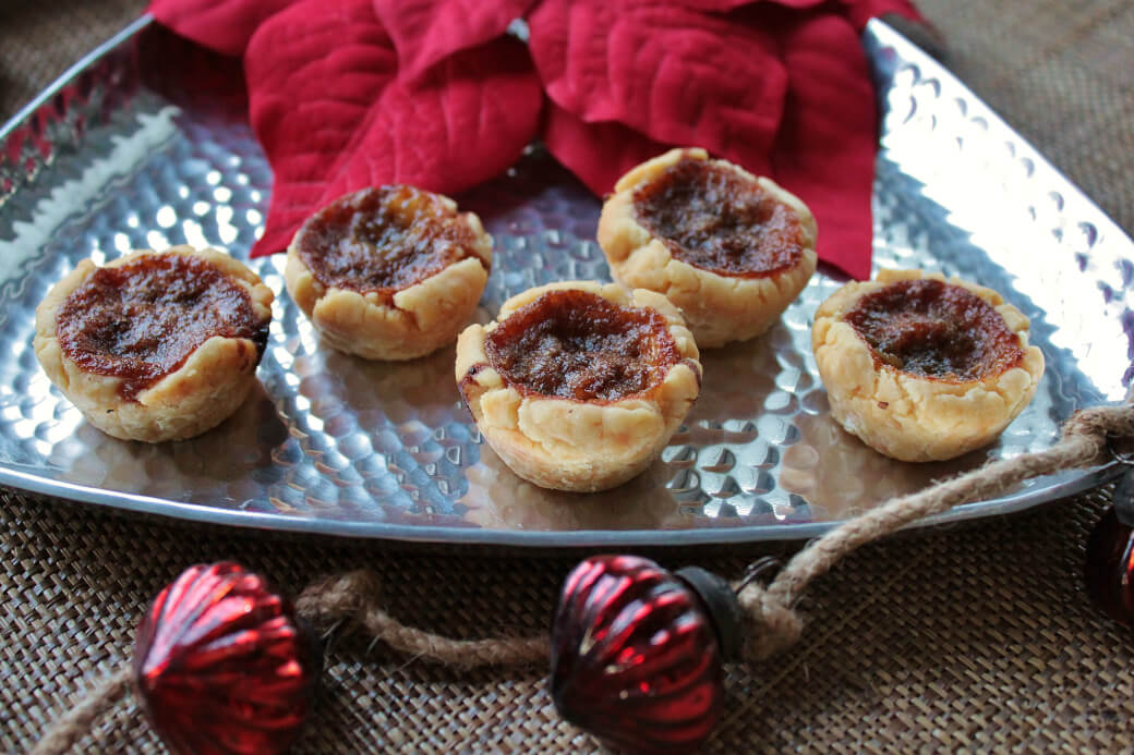 Butter Tarts on a silver serving tray surrounded by a red poinsetta and Christmas decorations. 