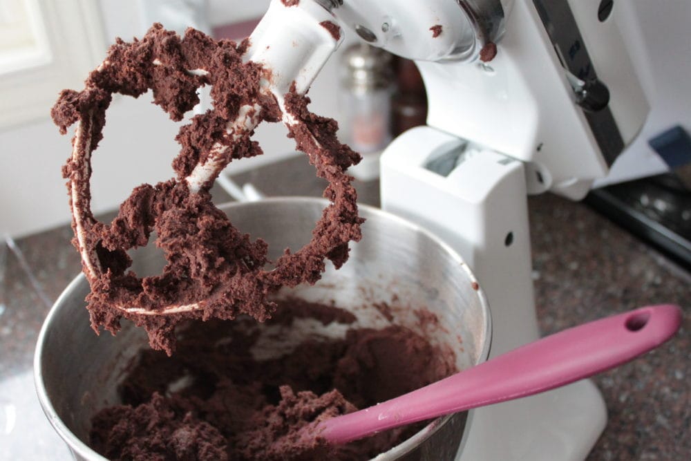 A white stand mixer bowl full of dark chocolate cookie dough. 