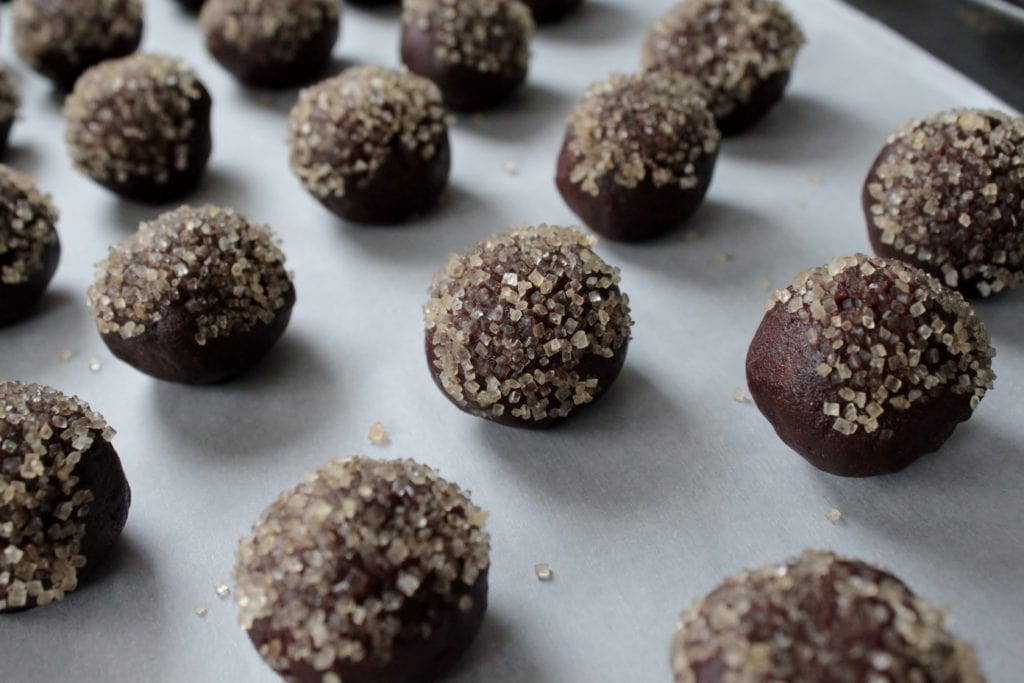Bailey's Thumbprint Cookies Rows of dark chocolate cookie balls topped with sugar crystals sit on parchment paper. 