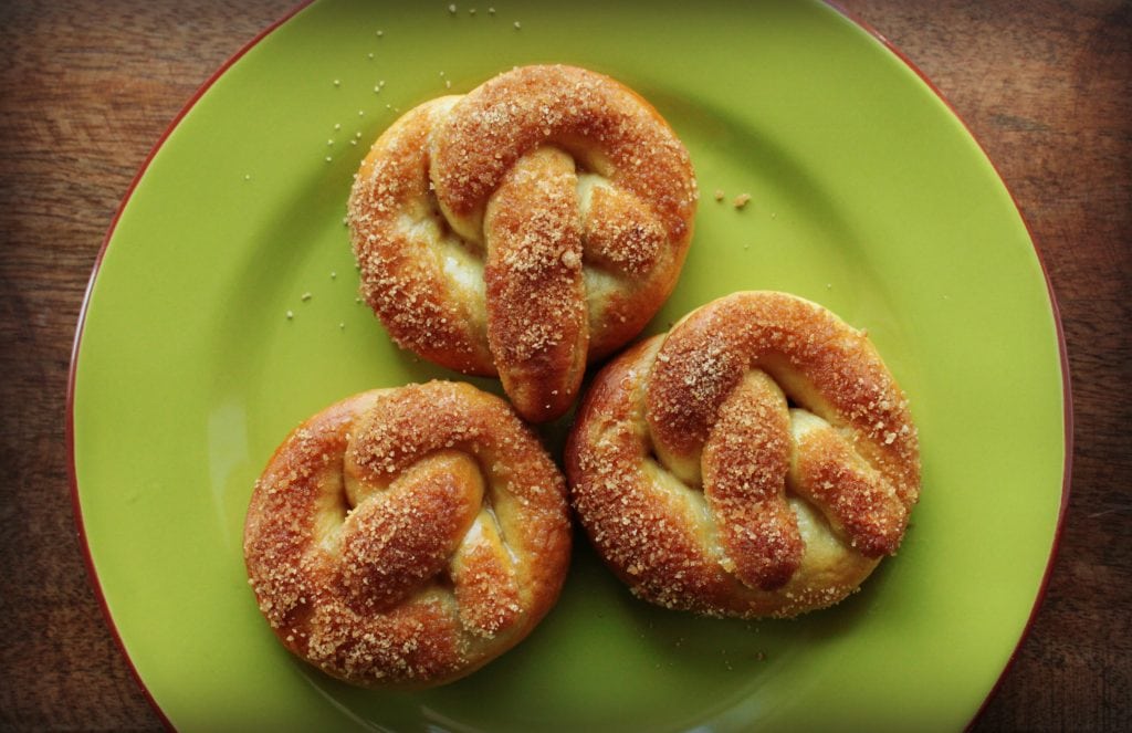 Golden baked soft pretzels topped with cinnamon sugar on a green plate.