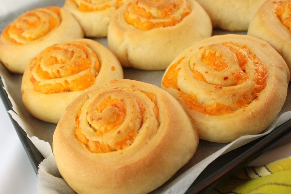 Cheesebuns - Close up of a round scrolled baked bun filled with cheddar cheese.