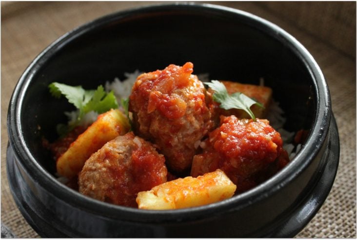 Saucy sweet and sour meatballs and pineapple in a black serving dish.