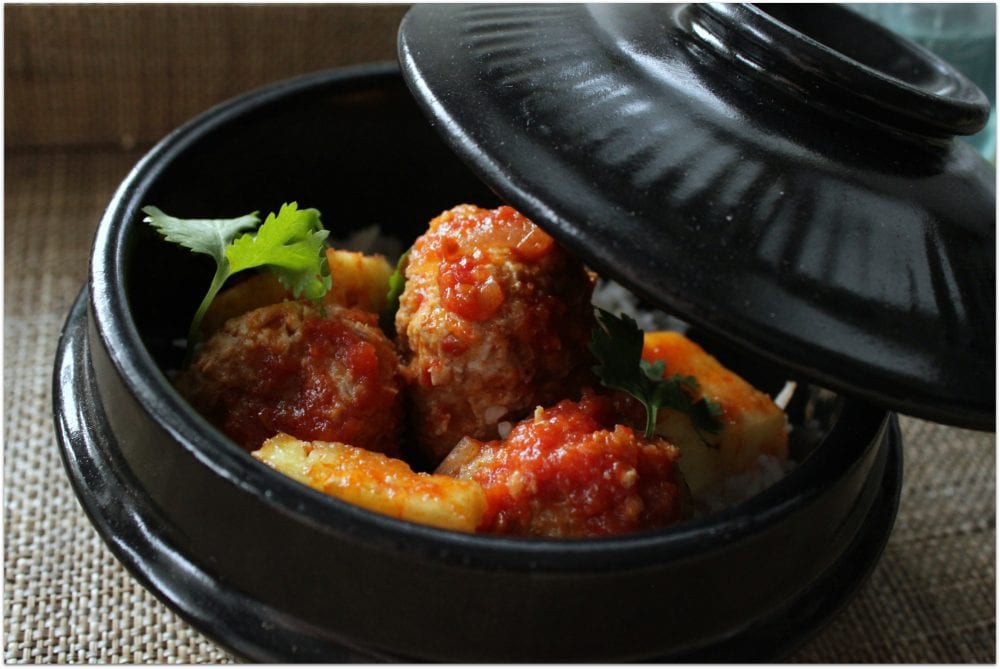 Saucy sweet and sour meatballs and pineapple in a black serving dish.