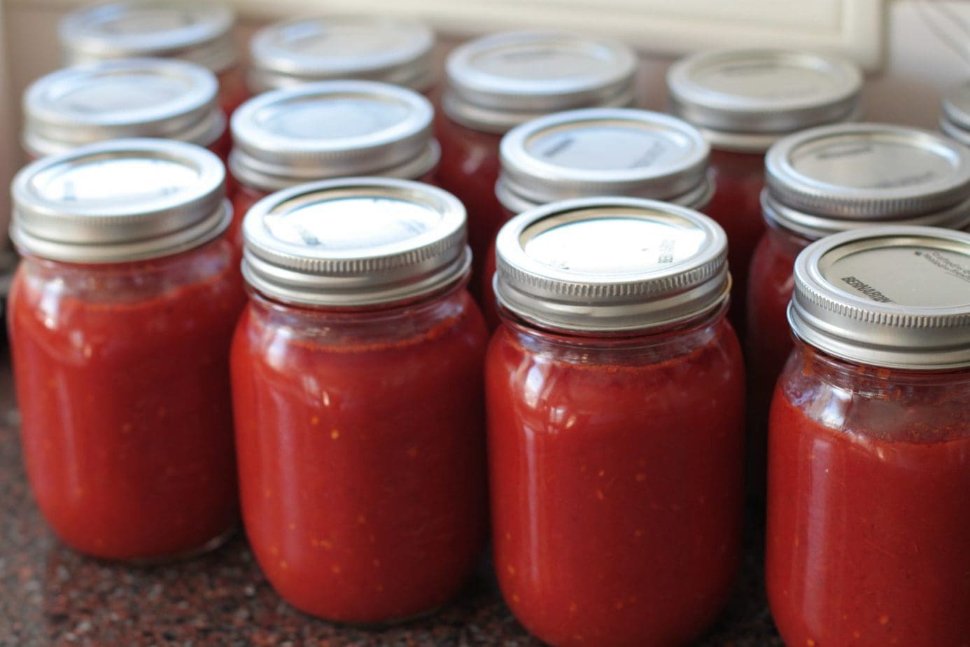Jars of bright red Roma Tomato Passata Sauce on a kitchen counter.