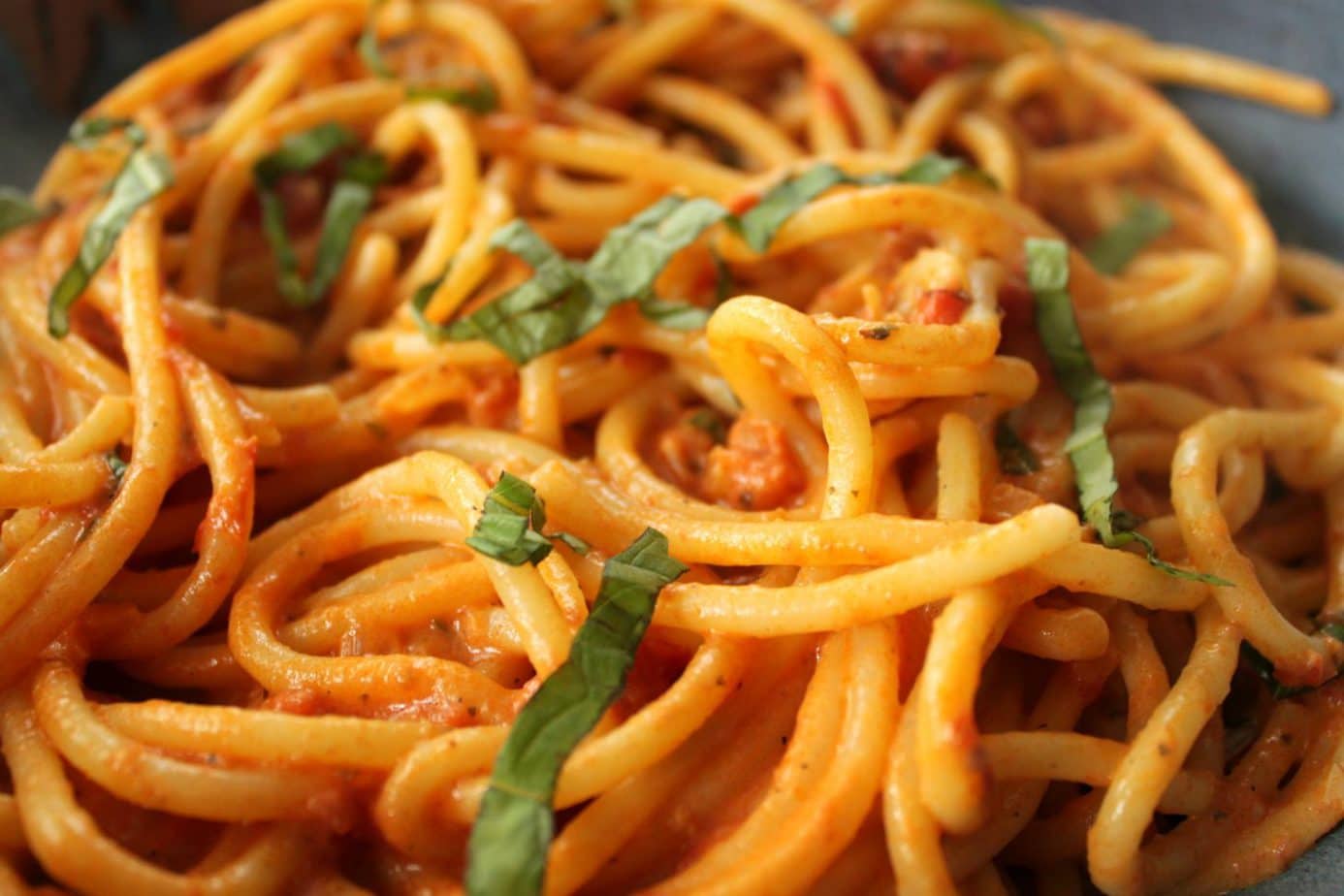 A plate of cooked bucatini pasta coated in a rose vodka sauce and garnished with fresh basil.