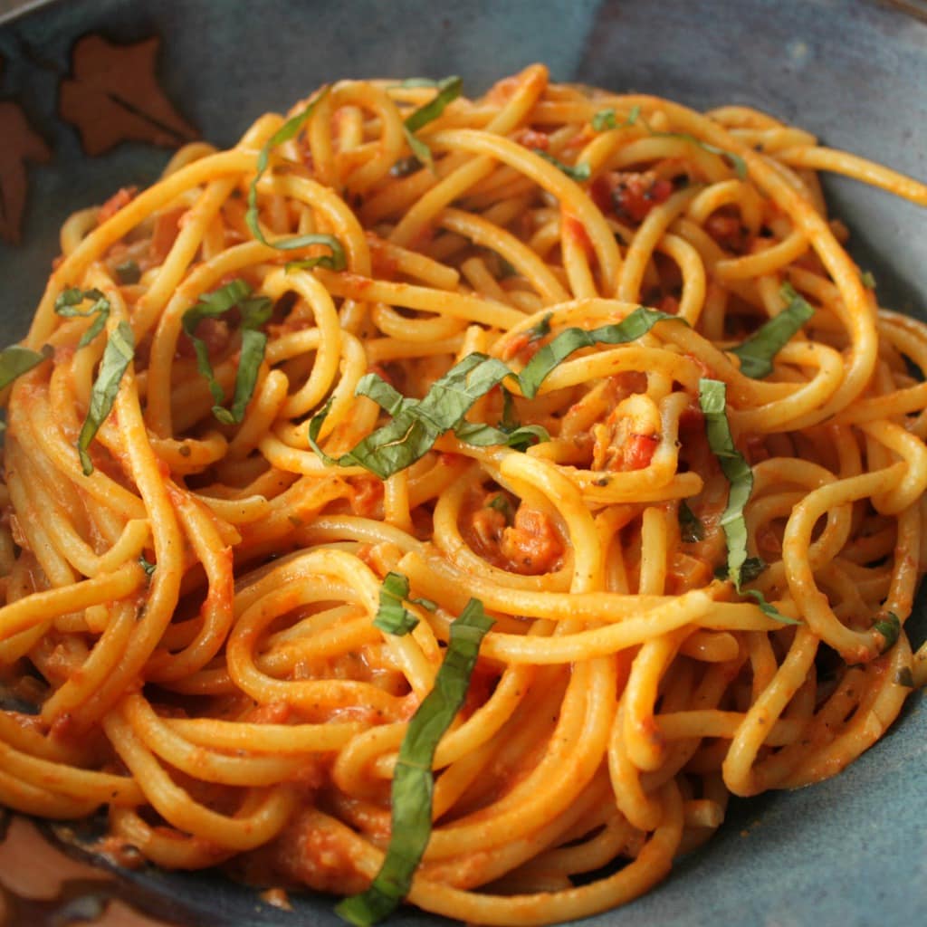 A plate of cooked bucatini pasta coated in a rose vodka sauce and garnished with fresh basil.