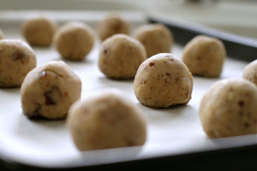 Noël Balls-Shortbread cookie balls wait to be baked on a parchment lined baking sheet. 