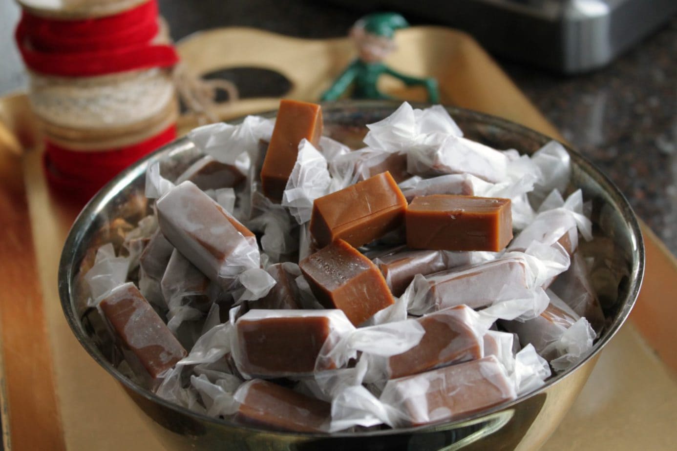 Apple Cider Caramels wrapped in wax paper in a silver bowl.