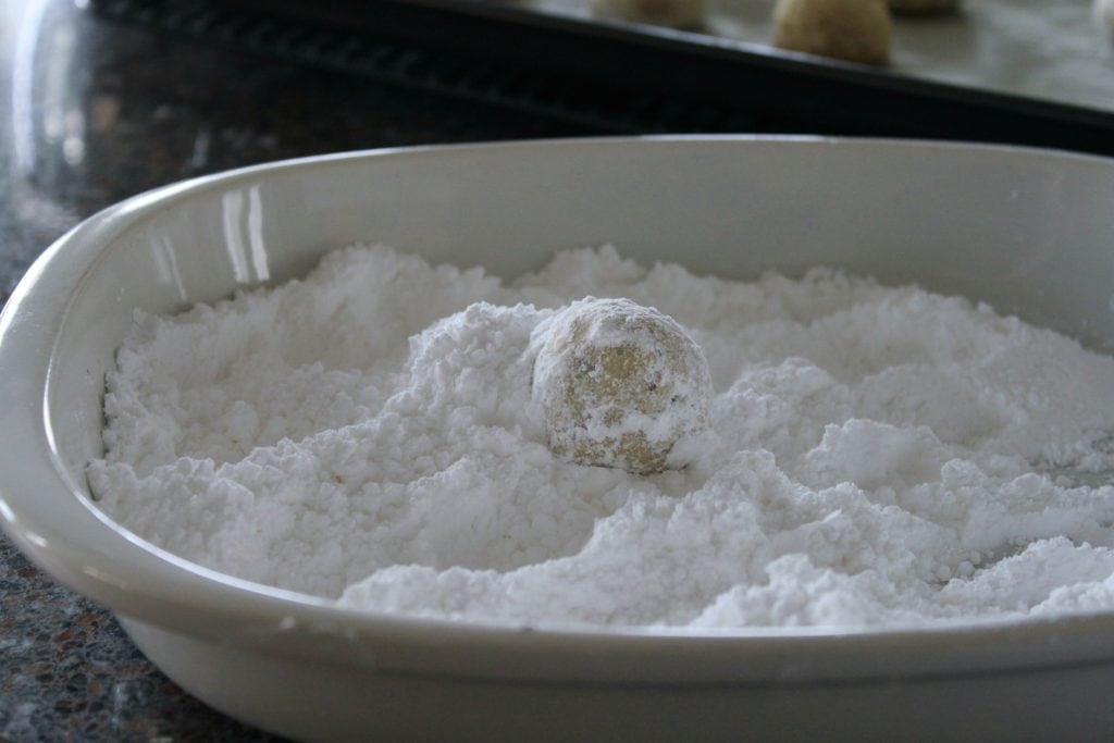 Noël Balls-A shortbread cookie ball being rolled in powdered sugar. 