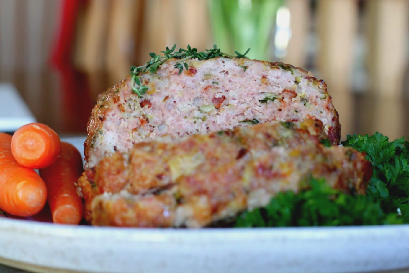 Close up of a sliced pork meatloaf topped with thyme and surrounded by carrots and kale.