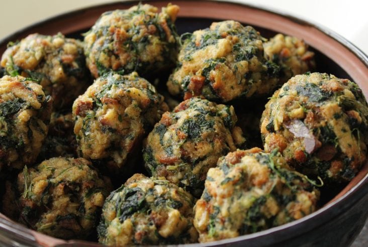 A bowl full of baked stuffing balls dotted with spinach.