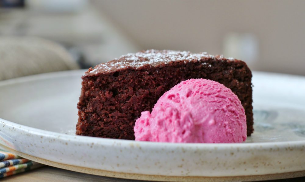 A slice of chocolate beet cake with a scoop of vibrant pink beet and orange ice cream.
