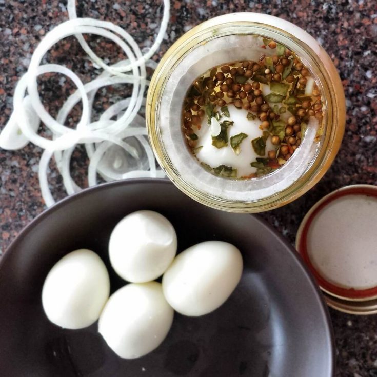 A jar of pickling spices, some onions, and some hard boiled eggs.