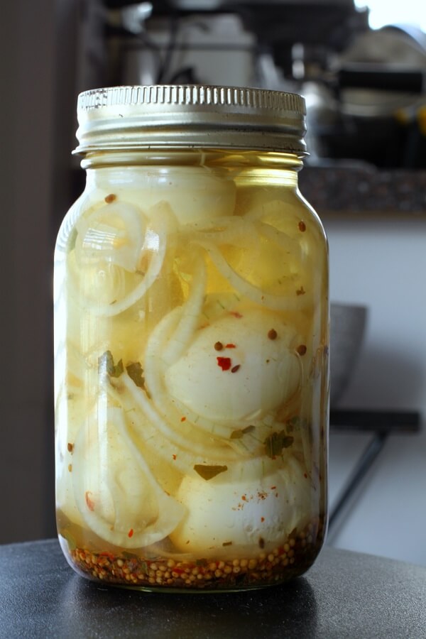 A jar containing eggs, pickling spices, and onions.