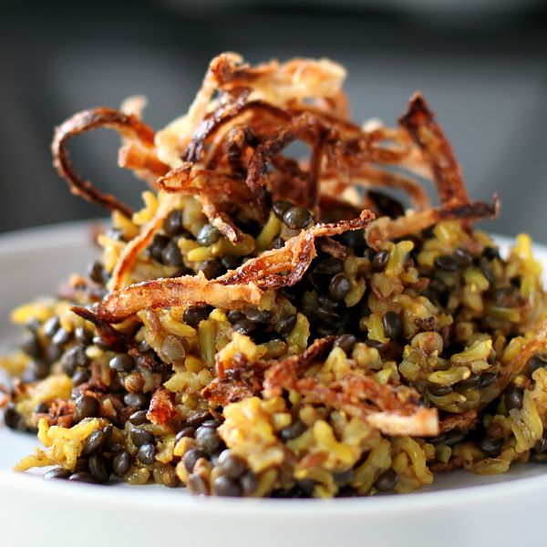 Mejadra - A white bowl filled with rice and lentils topped with golden fried onions.