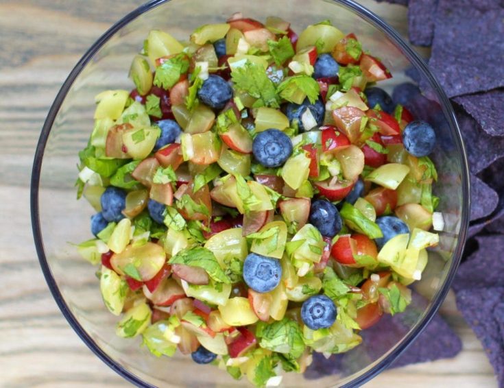 A bowl full of salsa made from chopped green and red grapes with blueberries and cilantro.