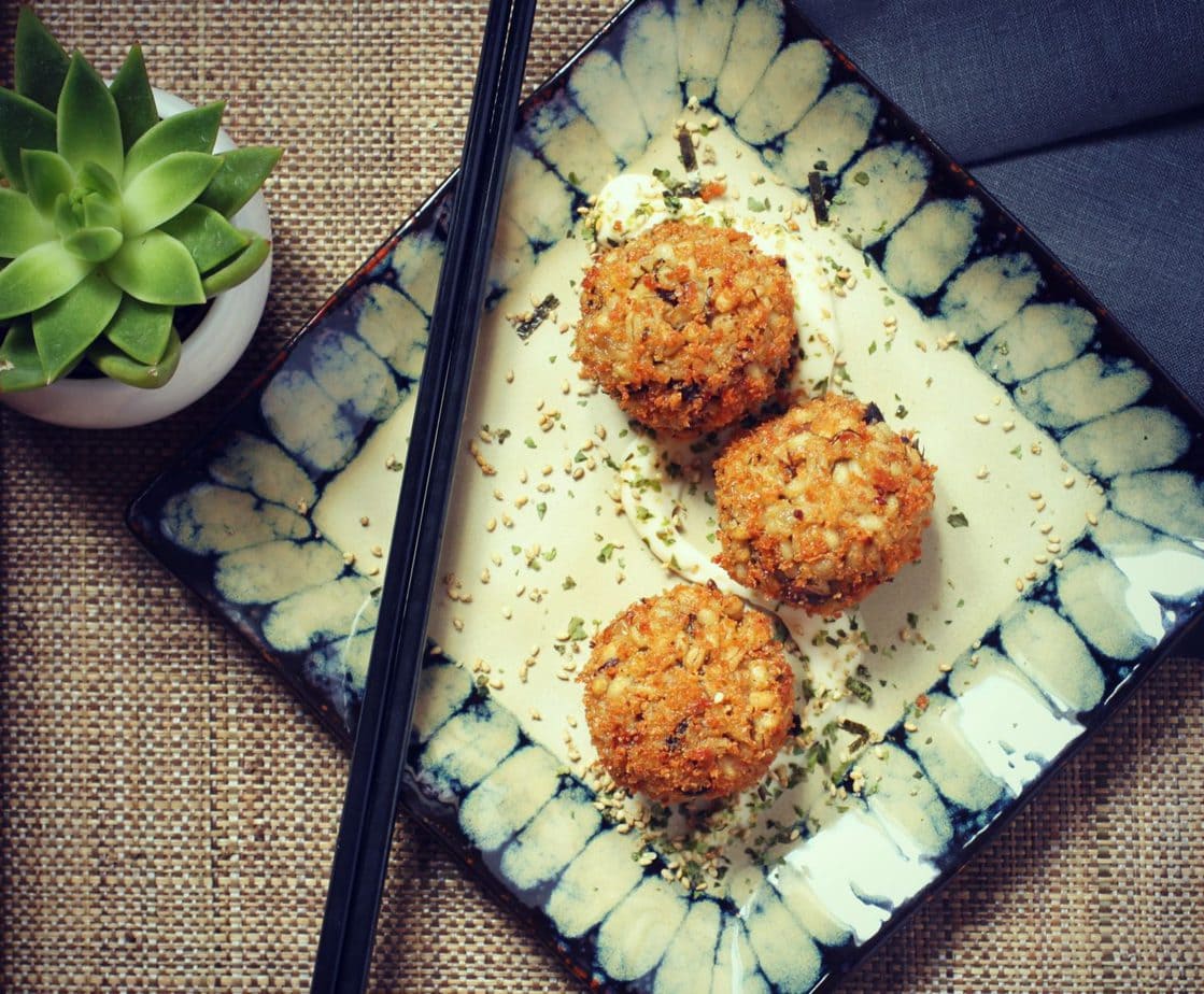Three Golden balls of Barley Arancini with Shiitake Mushrooms & Seaweed on a square plate.