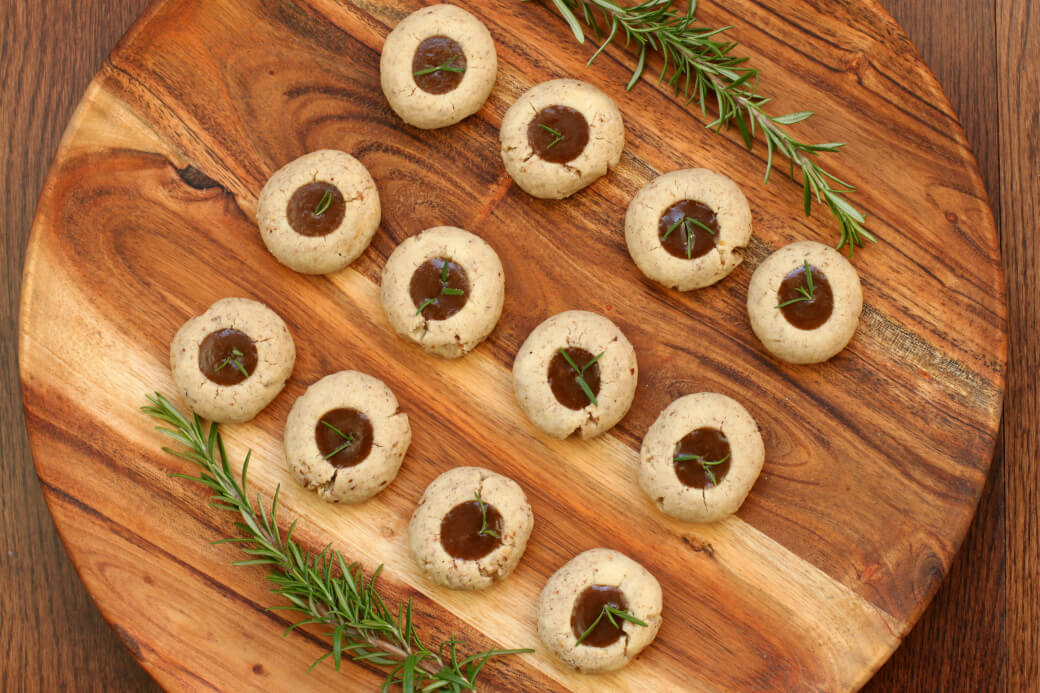 Pecan Polvorones - Caramel filled cookes topped with a sprig of green rosemary on a wooden platter.