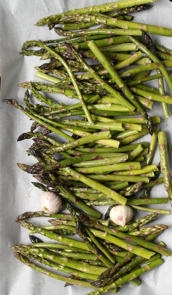 Bright green asparagus and garlic cloves in a roasting pan. 