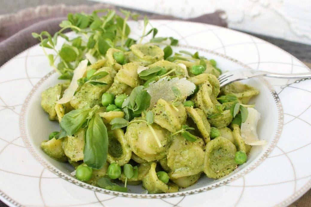 A side view of a bright green pasta dish featuring spring peas and shoots with orecchiette pasta.