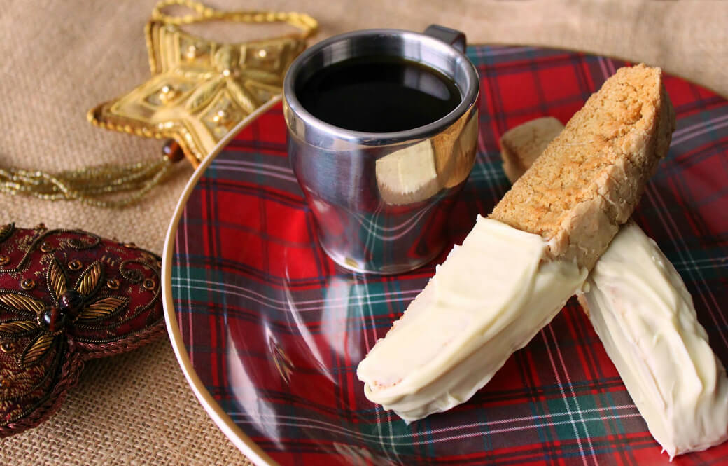 Cookinotti Biscotti - Two white chocolate dipped biscotti sit on top of a plaid plate with a cup of espresso.