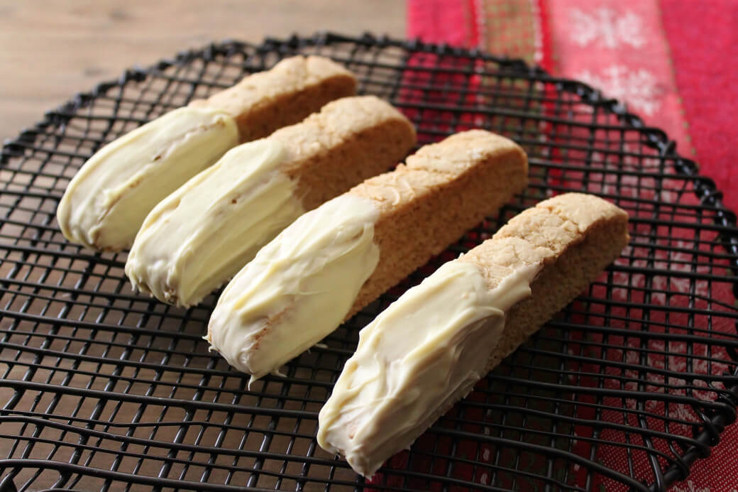 Cookinotti Biscotti - Four white chocolate dipped biscotti sit on top of a black cooling rack. 
