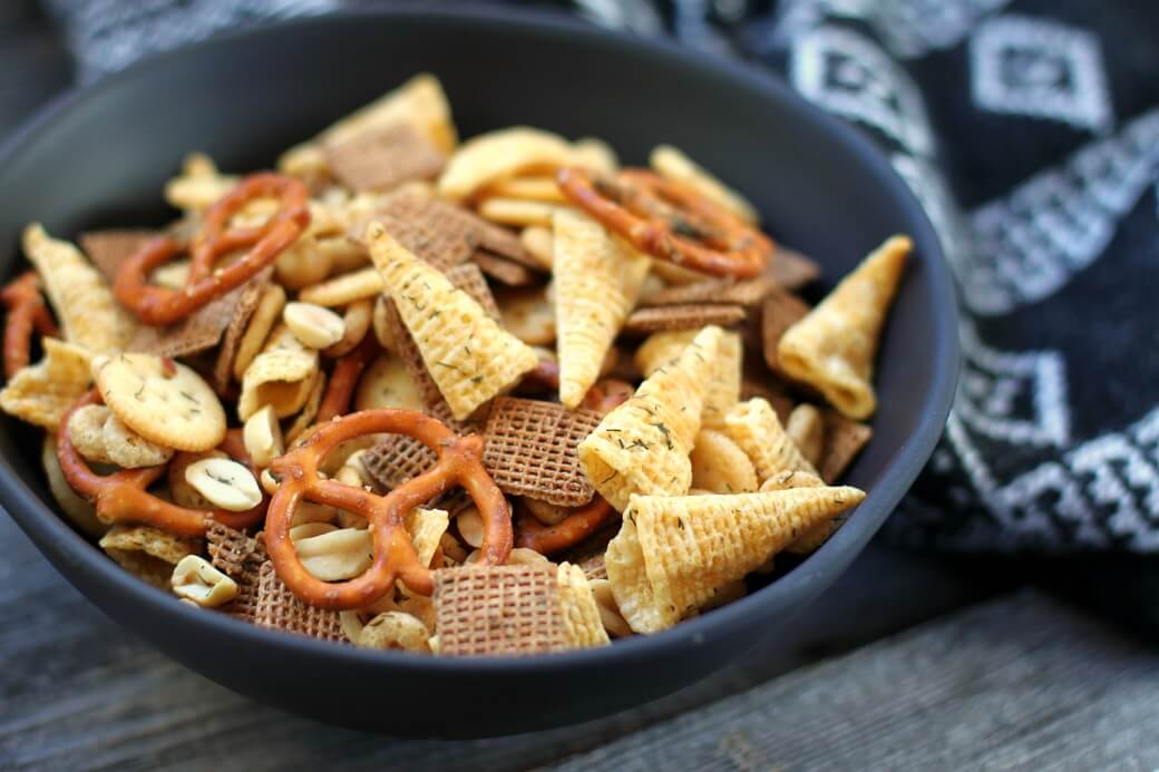 Ranch Nuts 'n' Bolts -Dish 'n' the Kitchen A black bowl of mixed cereals, nuts, and chips sits surrounded by playing cards and a napkin.