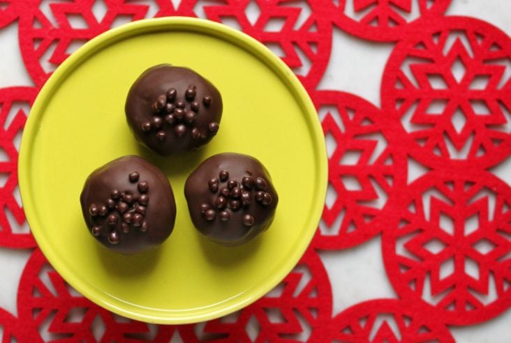 Three chocolate covered Nanaimo Truffles on a bright green plate sit on a red doily.