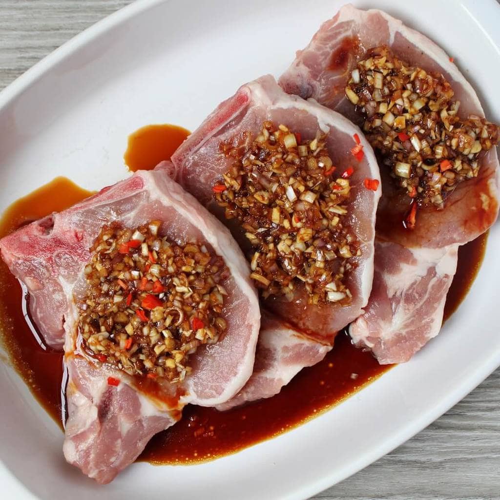 Three raw Pork Chops covered with a fresh lemongrass based marinade.