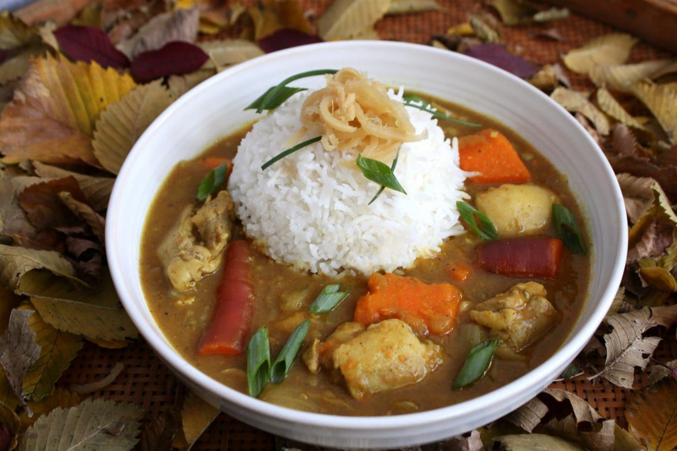 A white bowl of Japanese chicken curry with a side of rice and ginger pickles.