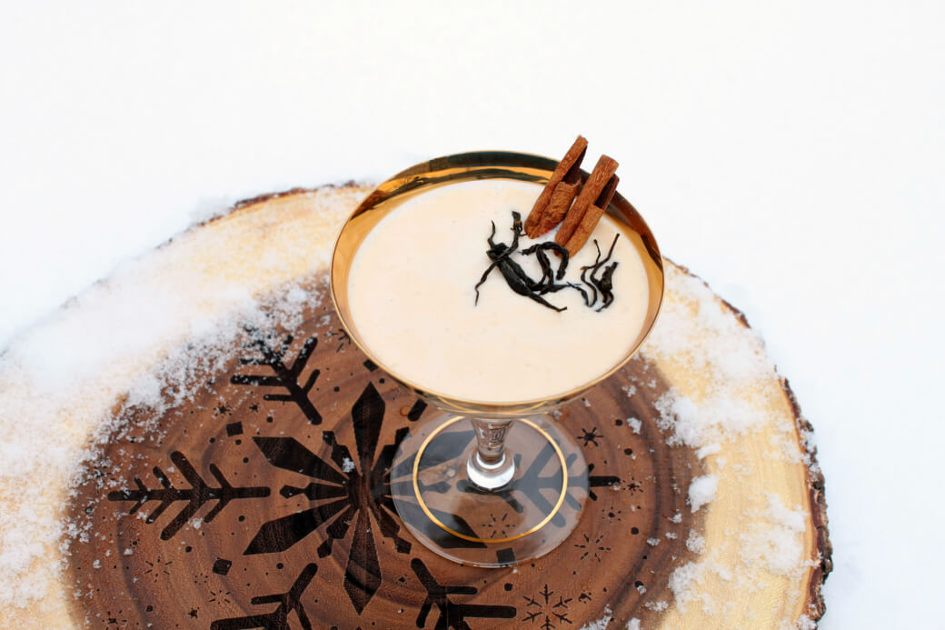 Dirty Chai Cocktail - A gold rimmed coupe glass holds a creamy cocktail garnished with cinnamon sticks and black tea.