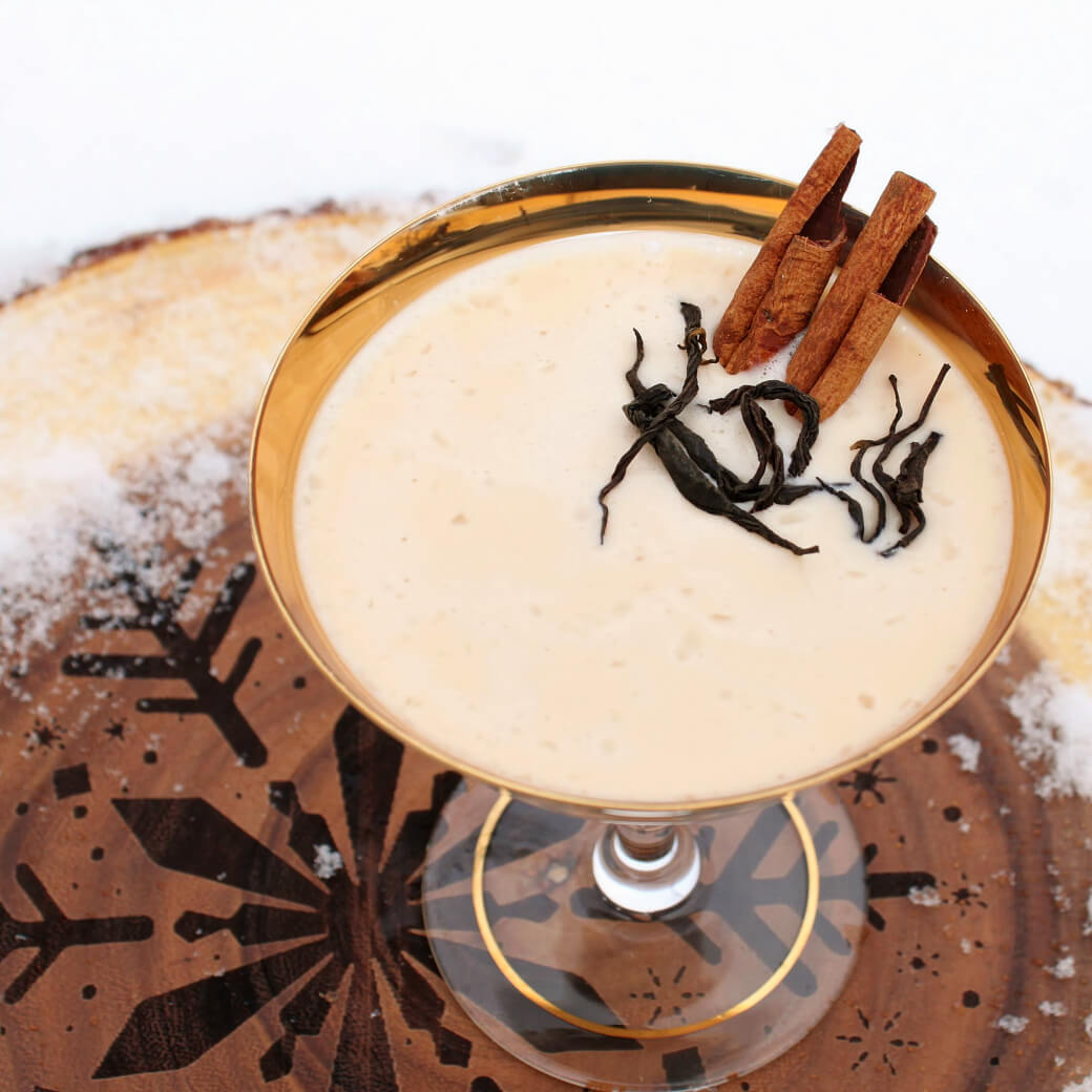 Dirty Chai Cocktail - A gold rimmed coupe glass holds a creamy cocktail garnished with cinnamon sticks and black tea.