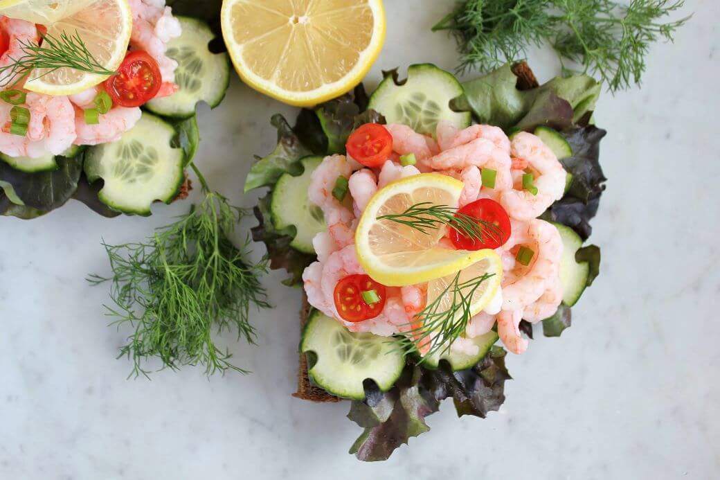 An open faced shrimp sandwich made with fresh toppings beautifully arranged on a piece of rye bread.