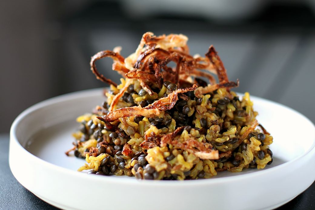 Mejadra - A white bowl filled with rice and lentils topped with golden fried onions.