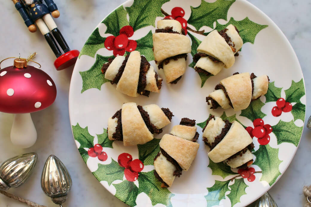 Rugelach - Seven rugelach arranged on a Christmas plate surrounded by Christmas decorations. 