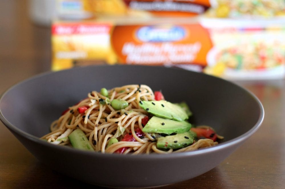 A Chilled Soba Noodle Salad with avocados, red peppers, and sesame seeds in a brown bowl.
