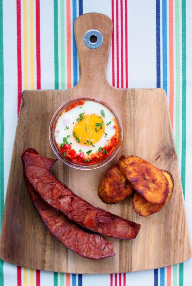A vibrant photo featuring Huevos Habaneros, a typical Cuban breakfast of baked eggs in tomato sauce, chorizo sausage, and fried plantains.