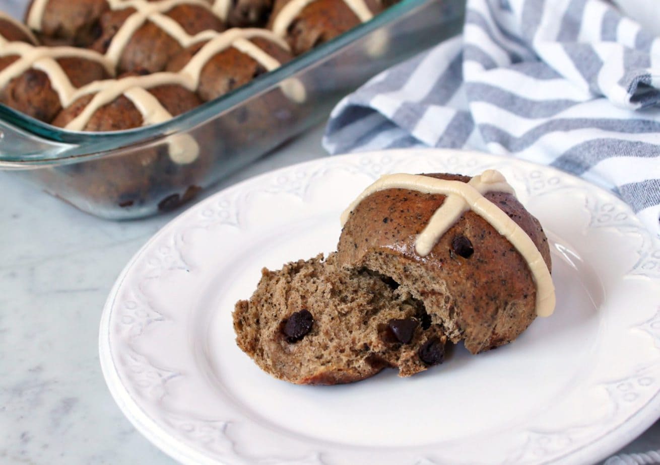 Mocha and Chocolate Chip Sourdough Hot Cross Buns - A glass baking dish full of hot cross buns and a single bun on a white plate.