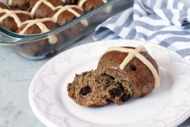 Mocha and Chocolate Chip Sourdough Hot Cross Buns - A glass baking dish full of hot cross buns and a single bun on a white plate.