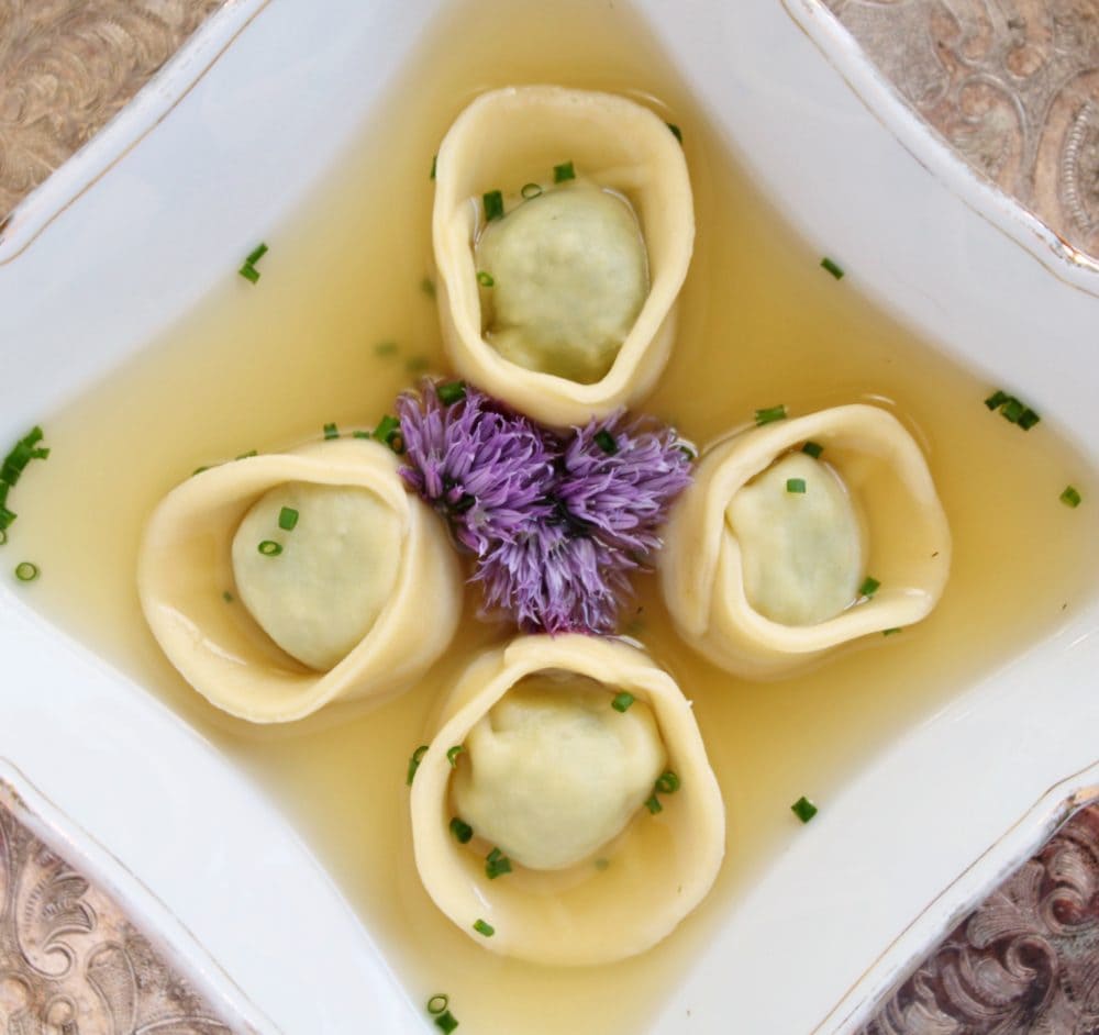 A bowl with four homemade tortellini in broth.