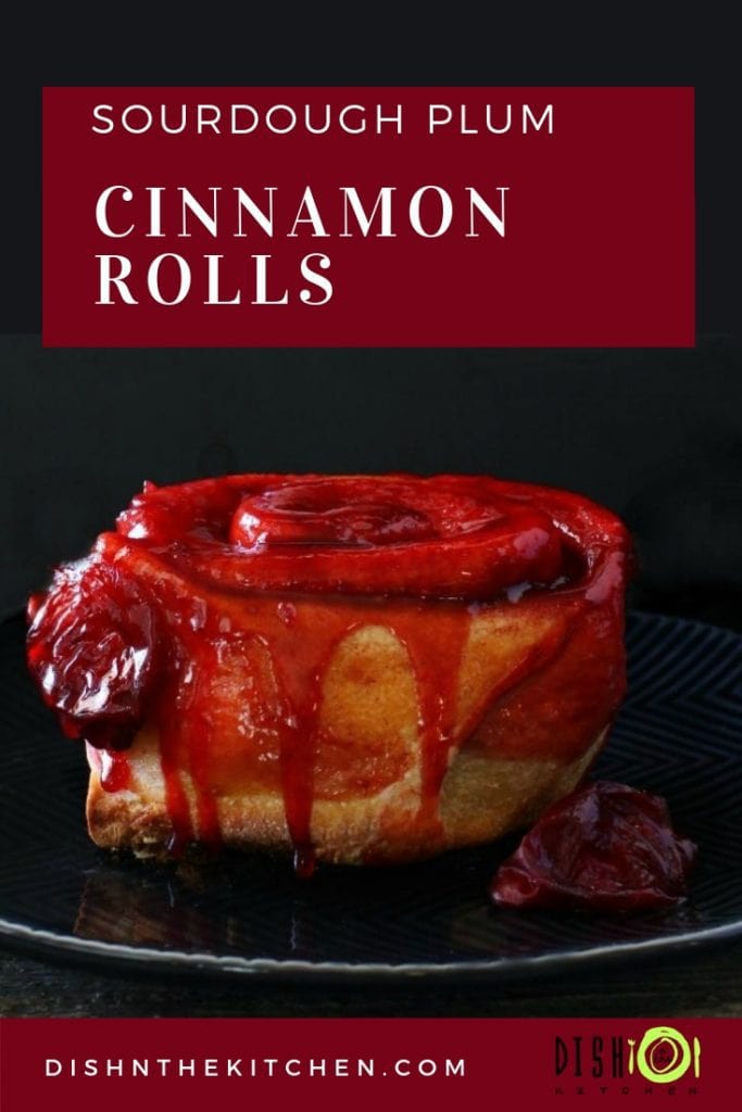 Sourdough Plum Cinnamon Rolls - A Baked cinnamon roll dripping with bright red plum juice on a black plate. 