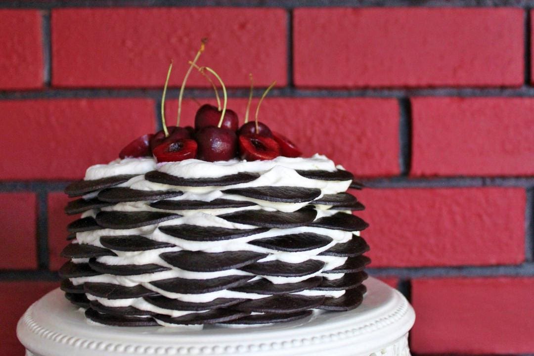 A chocolate biscuit cake with layers of biscuits and whipped cream topped with fresh cherries.